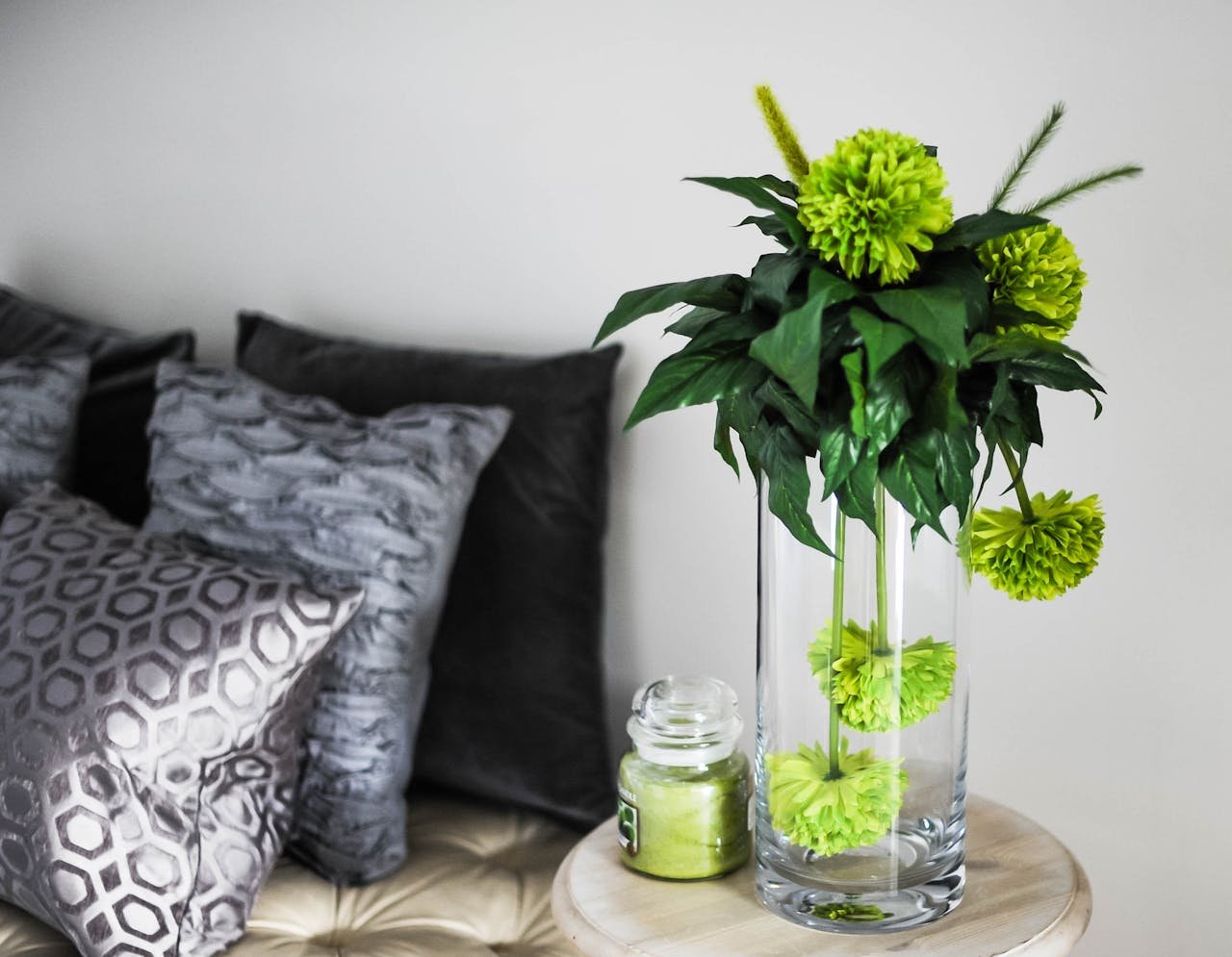 Sophisticated room decor featuring green flowers in a vase, soft pillows, and chic glass jar.