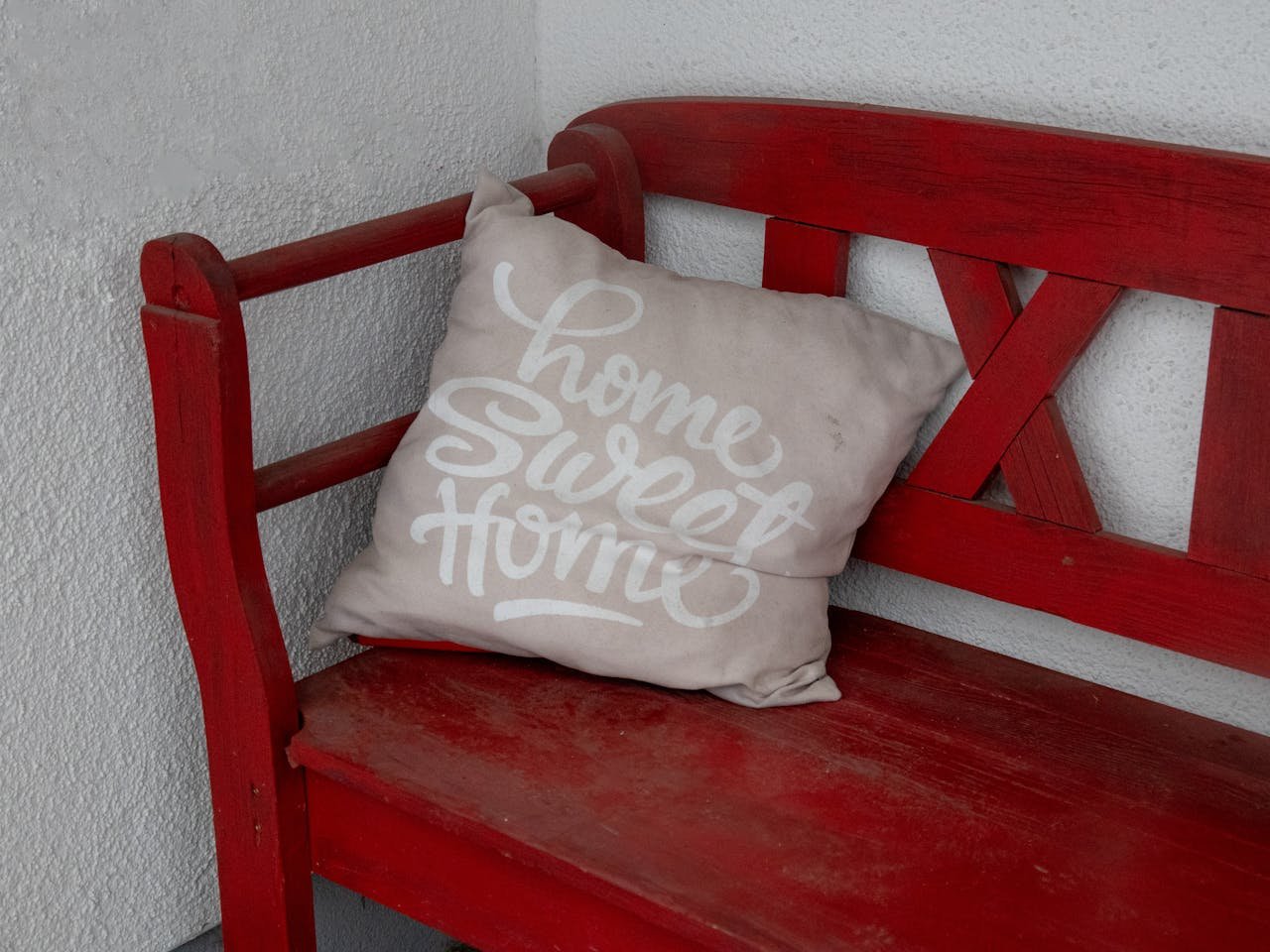 A beige cushion with Home Sweet Home text rests on a vintage red bench indoors.