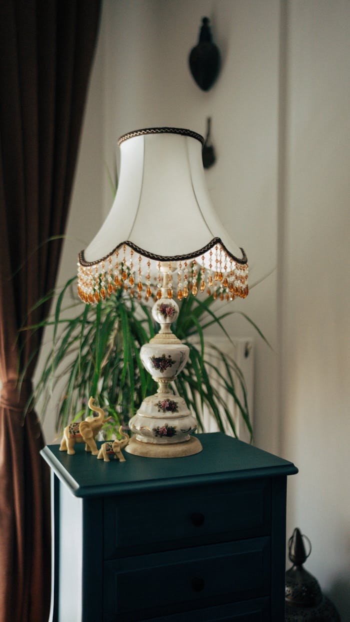 Elegant vintage table lamp with intricate beading on wooden cabinet.